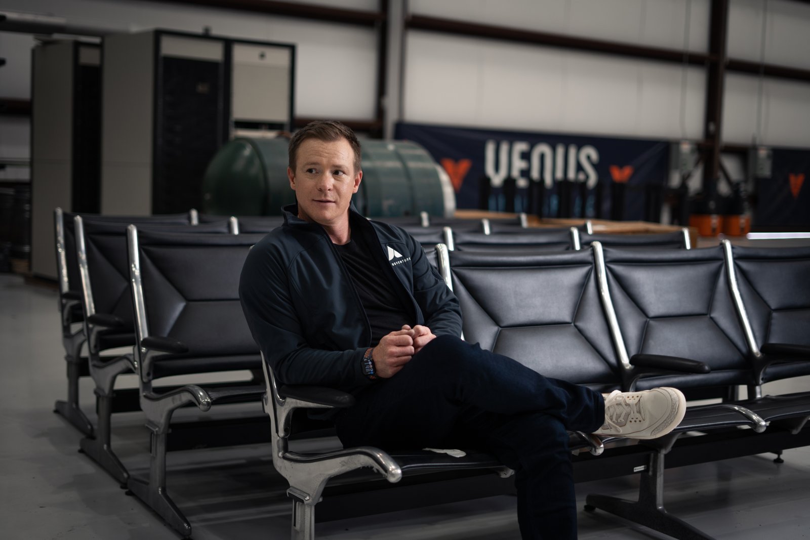 Curt Steinhorst seated in the Venus Aerospace hangar, Venus banner behind him